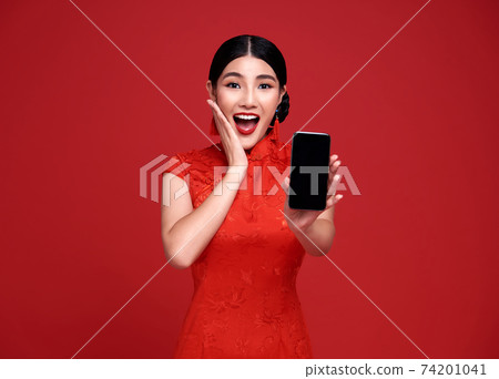 Excited Asian woman wearing traditional cheongsam qipao dress showing mobile phone Excited Asian woman wearing traditional cheongsam qipao dress showing mobile phone 74201041