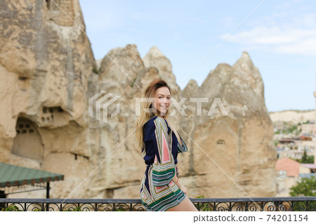 Caucasian smiling girl standing with ancient cave town on backround in Cappadocia, Turkey. 74201154