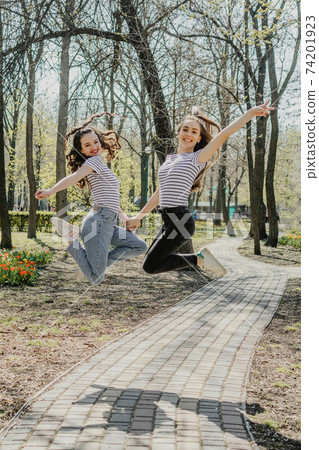 Gen z girls enjoying outdoors, expressing positive emotions. Outdoor photo of two girl friends having fun in the park. Two happy joyful young women jumping and laughing together Gen z girls enjoying outdoors, expressing positive emotions. Outdoor photo of two girl friends having fun in the park. Two happy joyful young women jumping and laughing together 74201923