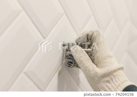Worker's hand in glove inserts wall pvc dowel in wall cladded with tile ceramic 74204156