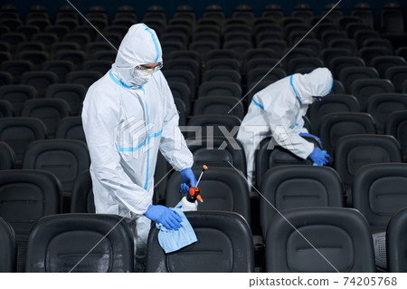 Two workers wiping chairs with disinfectants in cinema. Two workers wiping chairs with disinfectants in cinema. 74205768