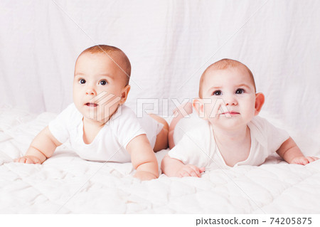 Two baby twins lying on the stomach at the white Two baby twins lying on the stomach at the white 74205875