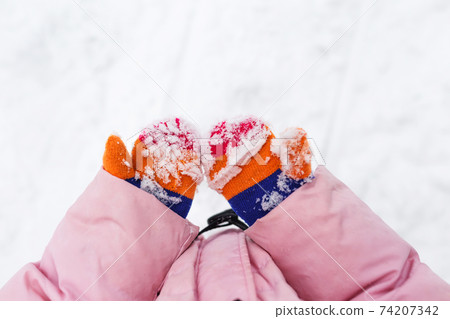 snow on mittens or gloves. Children's hands are holding hands in the snow. Colorful knitted winter mittens, stained with snow. Winter vacation. snow on mittens or gloves. Children's hands are holding hands in the snow. Colorful knitted winter mittens, stained with snow. Winter vacation. 74207342