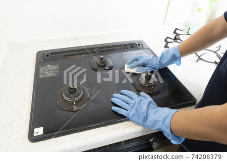 Hands of a male house cleaning worker cleaning a gas stove 74208379