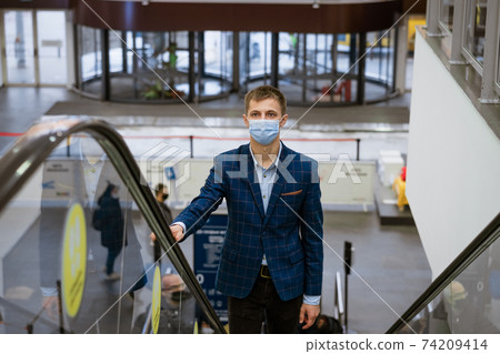 Young man wearing a mask climbs the escalator in the mall 74209414