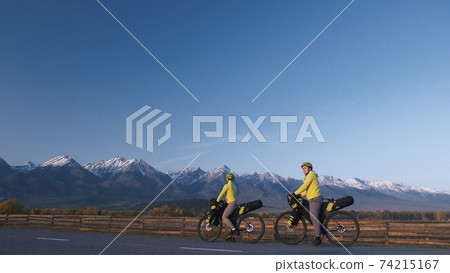 The man and woman travel on mixed terrain cycle touring with bikepacking. The love couple journey with tent in with bicycle bags. Stylish sportswear. The man and woman travel on mixed terrain cycle touring with bikepacking. The love couple journey with tent in with bicycle bags. Stylish sportswear. 74215167