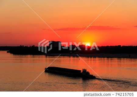 Tugboat pushing a heavy long barge on the river Dnieper at sunset Tugboat pushing a heavy long barge on the river Dnieper at sunset 74215705