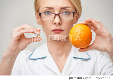 nutritionist doctor healthy lifestyle concept - holding fresh organic orange fruit and vitamin capsules 74224487