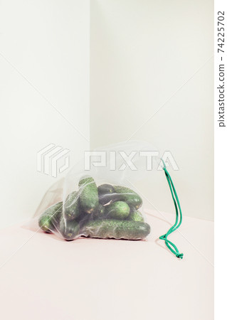 Reusable packaging of products by weight. Cucumbers in a reusable bag close up on a pink background 74225702