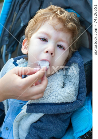 small child with mobility impairment eating a crushed in his adapted wheelchair. The mother feeds him with a spoon small child with mobility impairment eating a crushed in his adapted wheelchair. The mother feeds him with a spoon 74226651