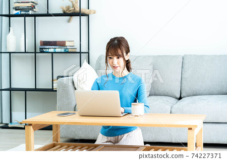 A woman using a laptop at a low table in the living room A woman using a laptop at a low table in the living room 74227371