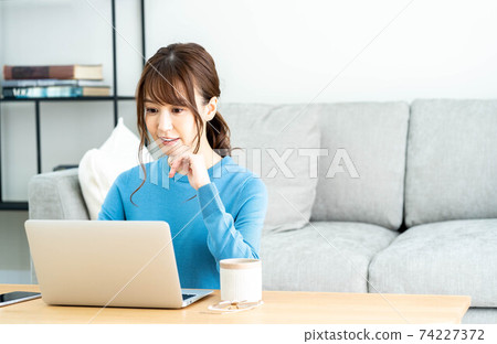 A woman using a laptop at a low table in the living room A woman using a laptop at a low table in the living room 74227372