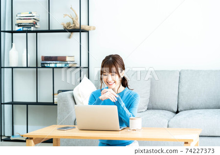 A woman using a laptop at a low table in the living room A woman using a laptop at a low table in the living room 74227373