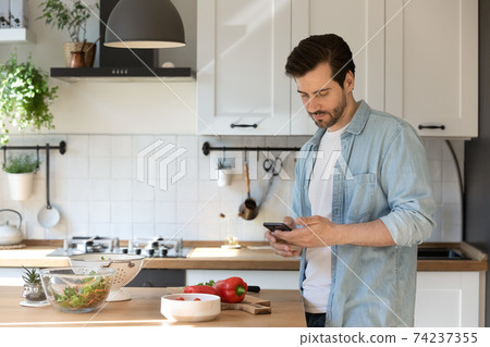 Millennial male preparing food holding smartphone ordering missing ingredients online 74237355