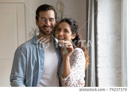 Portrait of happy newlyweds homeowners looking at camera showing keys Portrait of happy newlyweds homeowners looking at camera showing keys 74237379