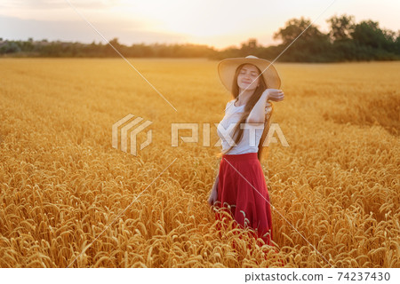 Young beautiful woman in hat standing among the stalks of ripe wheat. Tranquility Young beautiful woman in hat standing among the stalks of ripe wheat. Tranquility 74237430