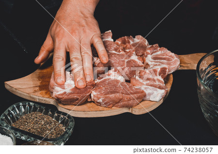 A man on a wooden board cuts pork into large pieces, close-up shows how to cut pork neck on a barbecue. A man on a wooden board cuts pork into large pieces, close-up shows how to cut pork neck on a barbecue. 74238057