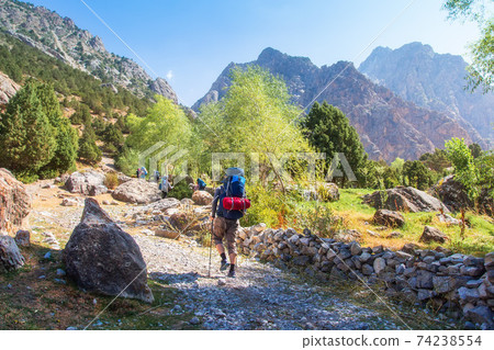 Group tourists with backpacks hiking in Fann mountains in Tajikistan. Hikers on mountain trail in Pamir. Adventure during trekking in mountains. Group tourists with backpacks hiking in Fann mountains in Tajikistan. Hikers on mountain trail in Pamir. Adventure during trekking in mountains. 74238554