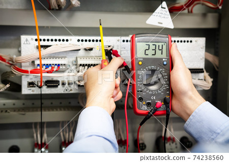 Electrician with multimeter in hands measures voltage in the electrical box. 74238560