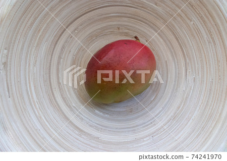 One single whole mango fruit of red and green colors in a bamboo dish top view One single whole mango fruit of red and green colors in a bamboo dish top view 74241970