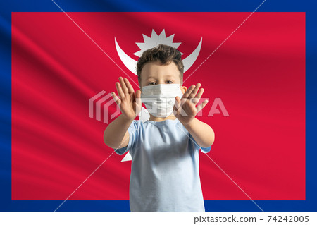 Little white boy in a protective mask on the background of the flag of Nepal. Makes a stop sign with his hands, stay at home Nepal 74242005