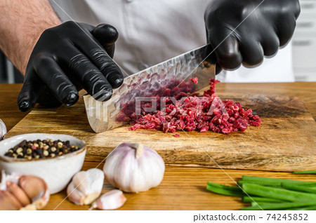 Man cutting raw beef meat. A chef in black gloves. Concept of cooking beef tartare Man cutting raw beef meat. A chef in black gloves. Concept of cooking beef tartare 74245852