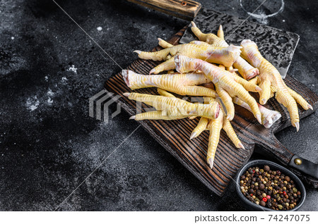 Raw Chicken feets on butcher cutting board with cleaver. Black background. Top view. Copy space 74247075