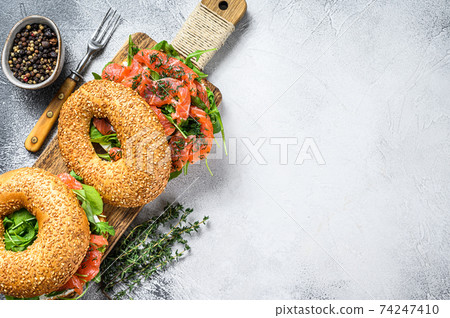Smoked salmon bagels sandwich with soft cheese and arugula on a cutting board. White background. Top view. Copy space 74247410