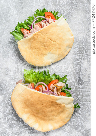 Doner kebab with grilled chicken meat and vegetables in pita bread. Gray background. Top view Doner kebab with grilled chicken meat and vegetables in pita bread. Gray background. Top view 74247476