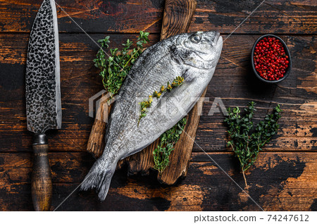 Raw dorado fish on a cutting board with knife. Dark wooden background. Top view 74247612