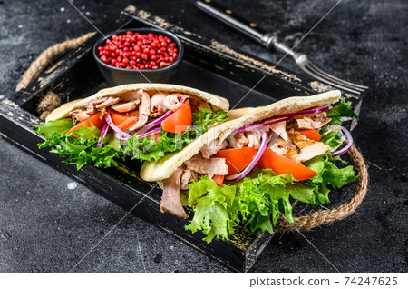 Doner kebab with grilled chicken meat and vegetables in pita bread on a wooden tray. Black background. Top view Doner kebab with grilled chicken meat and vegetables in pita bread on a wooden tray. Black background. Top view 74247625