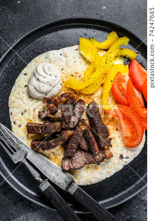 Tortilla with beef meat steak and fresh salad on a rustic plate. Black background. Top view Tortilla with beef meat steak and fresh salad on a rustic plate. Black background. Top view 74247685