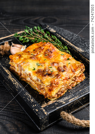 Portion of Lasagna with mince beef meat and tomato bolognese sauce in a wooden tray. Black wooden background. Top view Portion of Lasagna with mince beef meat and tomato bolognese sauce in a wooden tray. Black wooden background. Top view 74247803