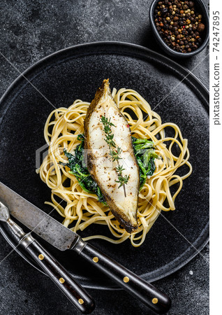 Spaghetti pasta with Halibut fish steak and spinach. Black background. Top view 74247895