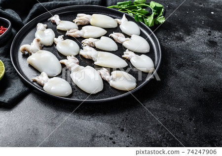 Fresh cuttlefish with rosemary and parsley on a plate. Black background. Top view. Copy space Fresh cuttlefish with rosemary and parsley on a plate. Black background. Top view. Copy space 74247906
