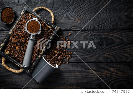 Ground Coffee in Portafilter for Espresso in a wooden tray with coffee beans. Black wooden background. Top view. Copy space Ground Coffee in Portafilter for Espresso in a wooden tray with coffee beans. Black wooden background. Top view. Copy space 74247952