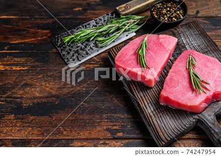 Raw tuna steaks on a wooden cutting Board with cleaver. Dark wooden background. Top view. Copy space 74247954