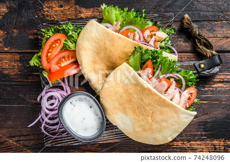 Greek gyros wrapped in pita breads with vegetables and sauce. Dark wooden background. Top view Greek gyros wrapped in pita breads with vegetables and sauce. Dark wooden background. Top view 74248096