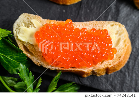 Red caviar in bowl and Sandwiches on stone board. Black background. Top view 74248141