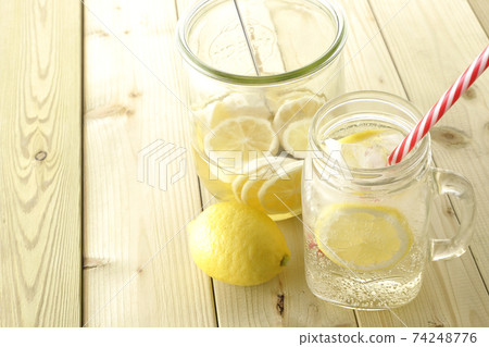 Lemon squash to drink in a Mason jar and undiluted solution and lemon in a storage container 74248776
