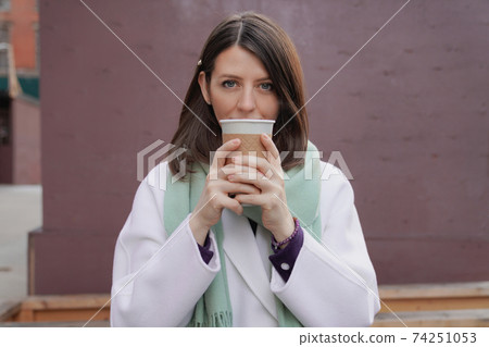 Smiling woman in winter coat with a coffee at the wall 74251053