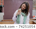 Smiling woman in winter coat with a coffee at the wall 74251054