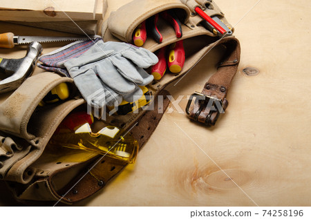Tool belt with carpenter tools and protective wear on plywood sheet 74258196