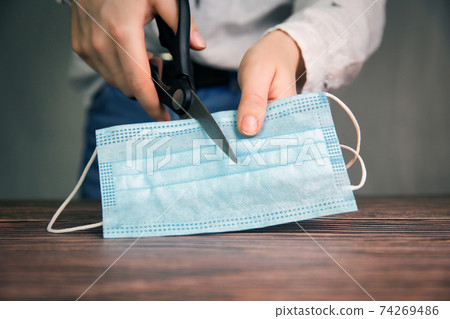Young Female hands cut a medical mask with scissors, protective facial mask for Covid-19 ,Concept for ending the lockdown and coronavirus pandemic. 74269486