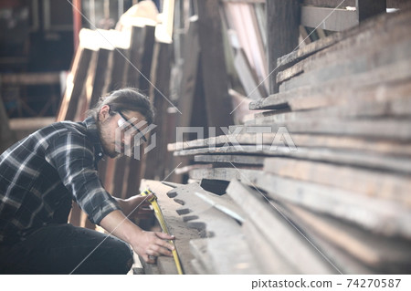 Carpenter, he is working in the workshop. Man at work on wood. Image of mature carpenter in the workshop, furniture making concept. Carpenter, he is working in the workshop. Man at work on wood. Image of mature carpenter in the workshop, furniture making concept. 74270587