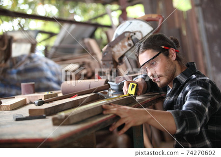Carpenter, he is working in the workshop. Man at work on wood. Image of mature carpenter in the workshop, furniture making concept. 74270602