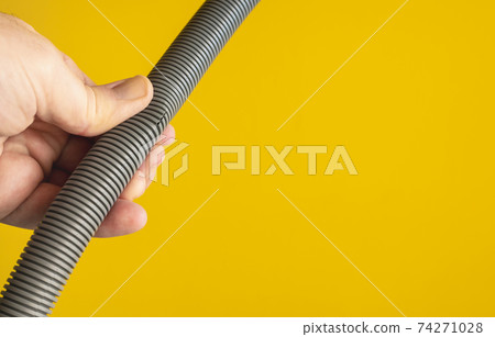 Against the yellow background the hands of a plumber are testing the integrity of a drain pipe: they highlight a crack that caused leaks and the replacement of the pipe. 74271028