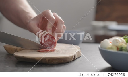 man slicing salame on olive wood board on concrete countertop 74276058