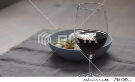 red wine into wineglass with bowl of fettuccine on background 74276063