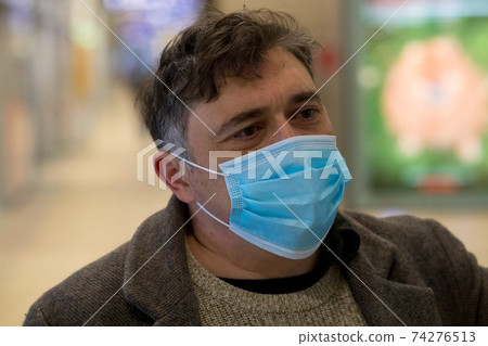 Disease outbreak, COVID-19 (Coronavirus SARS-CoV-2) pandemic. Headshot of a man covering his face with a medical mask to protect his nose and mouth 74276513